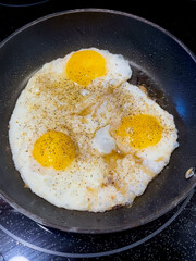 Three eggs sunny side up frying in a black non-stick pan