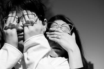 Conceptual portrait of a two women in eyeglasses. Young attractive women covering her faces with a her hands	
