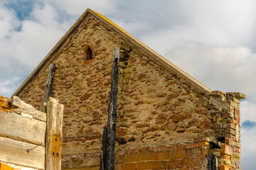Ściana szczytowa (z kamienia) zabytkowego spalonego domu. Stary zrujnowany wiejski dom wśród malowniczych pól na tle pochmurnego nieba w popołudnie pod koniec lata.