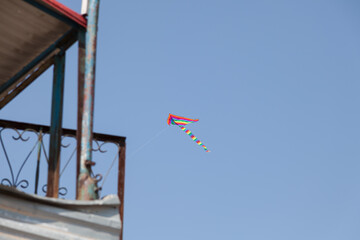 Multi-colored kite in the blue sky in windy weather.