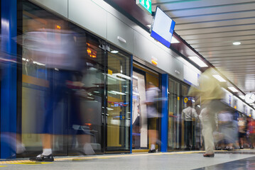 Commuters in fast motion blur rushing in and out of a subway train at a modern urban station..