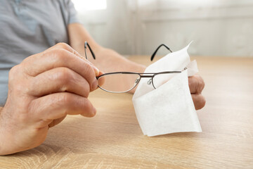 mature male hands carefully cleans glasses with thin metal frame, emphasizing vision health,...