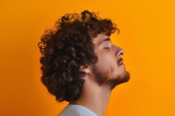 Side profile of a young man with curly hair against a vibrant orange backdrop