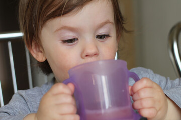 A small child drinks from a two-handed cup. Learning to drink from a cup independently. Developmental milestones and the joy of everyday family life