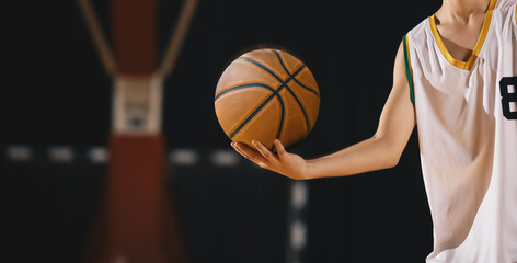 Young basketball player holds classic ball. Basket in background. Junior level basketball player...