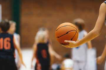 Young basketball player with classic basketball. Basketball training session for kids. Team players in blurred background. Junior level basketball player holding game ball