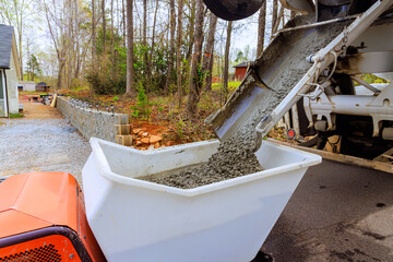 Construction site displays wet cement coming out of cement truck chute into concrete buggy driven...