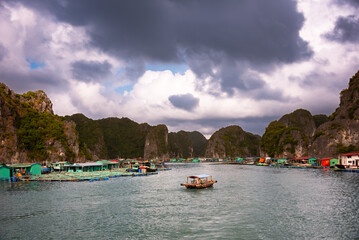 Floating fishing village in sea bay in Vietnam, boats and islands under dramatic sky - obrazy, fototapety, plakaty