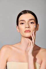 Obraz premium Brunette woman oozes elegance in a strapless dress, striking a pose with her hand delicately touching her face.