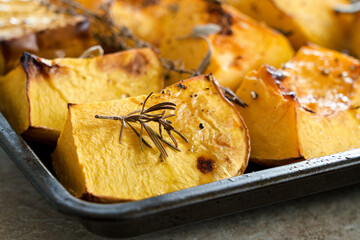 Pieces of organic oven roasted butternut squash in a baking sheet pan with fresh thyme and sage...