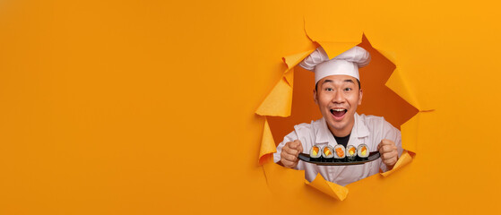 An excited chef wearing a white hat and uniform breaks through yellow paper, presenting sushi