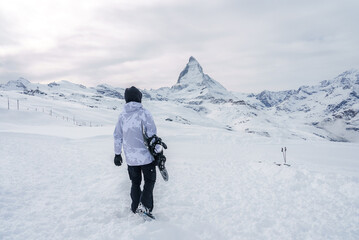 Snowboarder in camouflage winter gear walking towards Matterhorn peak in Zermatt ski resort,...