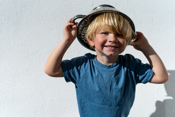 Little boy putting colander on his head . cheerful blond boy with a sieve on his head. positive kid