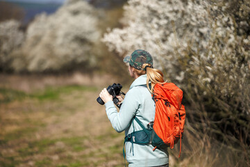 Bird watching. Woman ornithologist with binoculars observes birds arriving in spring in blooming nature
