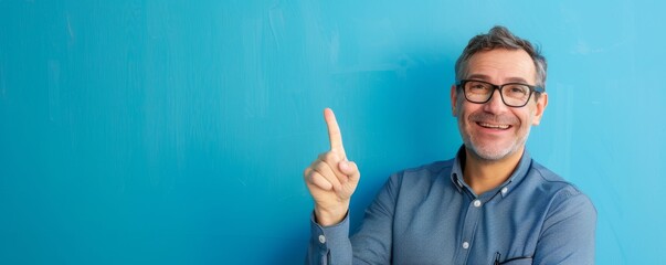 Smiling man pointing upwards on blue background - obrazy, fototapety, plakaty