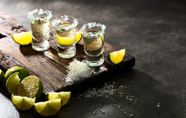 Tequila with sea salt and lime slices on a old cutting board.