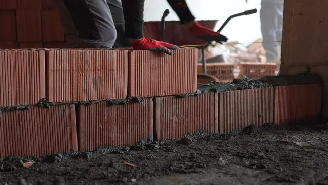 A construction worker laying bricks on cement to build a wall at the construction site, close-up.
