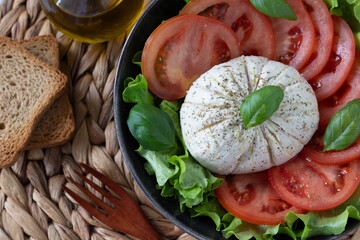 Vegan burrata cheese with fresh basil, tomato, lettuce, and olive oil on bamboo table. Top view. Close-up. Italian caprese mozzarella salad, healthy meal, Mediterranean food.