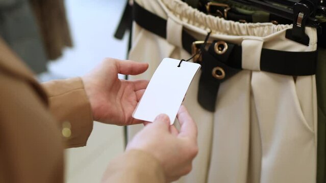 Woman is shopping for casual clothes, female's hands holding price tag mockup in clothing store, in boutique trying on clothes differents blouses quality of fabric. Shopping in Clothing Store.