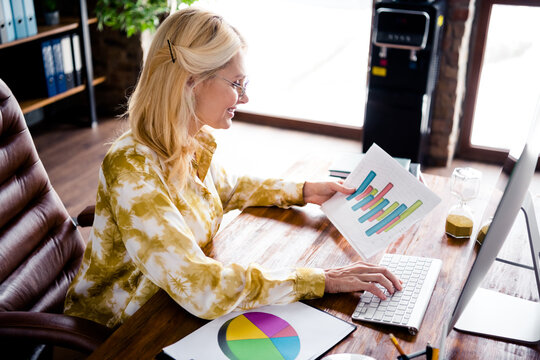 Portrait of successful lovely senior business lady sitting chair reading documents financial statistics graph workstation workspace - Powered by Adobe