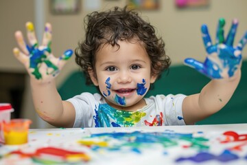 A curly boy preschooler toddler enjoys creative expression with finger paints, exploring color and texture while developing fine motor skills. - obrazy, fototapety, plakaty