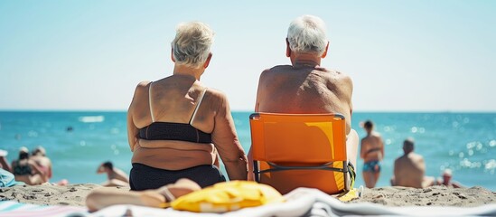 retired senior couple on summer vacation sunbathing on the beach - obrazy, fototapety, plakaty