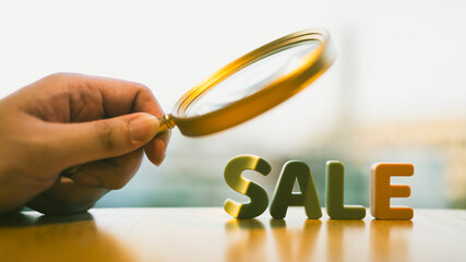 A woman who likes shopping is holding a magnifying glass with letters SALE, In order to choose products that are cheap and have quality.