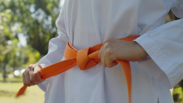 Cropped shot of unrecognizable taekwondo practitioner tying orange belt and preparing for training