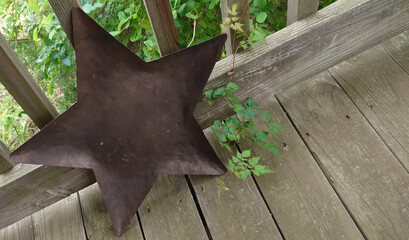 large rusty sheet metal star leaning against railing on wooden porch   - 781518950