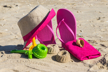 Different shapes made of sand, children toys for playing and accessories for relax. Straw hat, slippers and towel. Summer time on beach