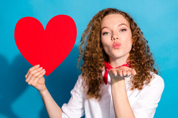 Photo of pretty young woman hold big red heart postcard send air kiss dressed stylish white clothes isolated on blue color background