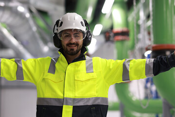 Portrait of handsome HVAC system engineer with green safety jacket and helmet working at machinery