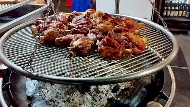 A large circular brazier with a grill on top full of pork shanks perfectly browned and ready to be eaten. Below, the still lit embers keep them warm.