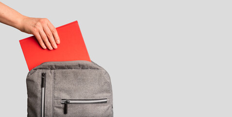 Hand putting red book, textbook into backpack, school bag. Banner background - obrazy, fototapety, plakaty