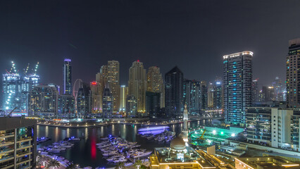 Fototapeta premium Yachts in Dubai Marina flanked by the Al Rahim Mosque and residential towers and skyscrapers aerial night timelapse.