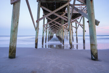 The view underneath an old rustic wooden fishing pier at sunset. Long exposure photo.