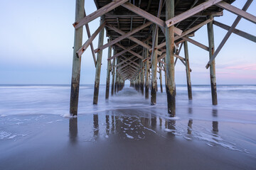 The view underneath an old rustic wooden fishing pier at sunset. Long exposure photo.