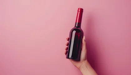 Fotobehang Female hand holding bottle of red wine on pink background © Oleksiy