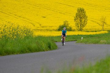 A young professional cyclist rides a bicycle quickly against the backdrop of blooming yellow...