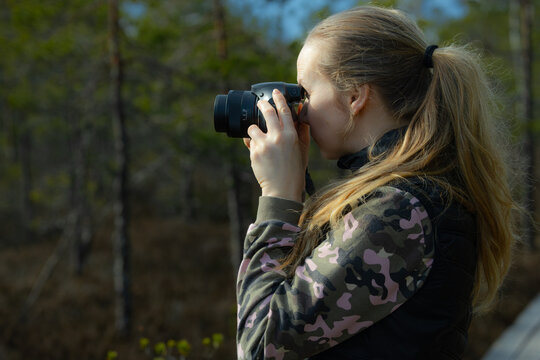A woman with a camera takes pictures of pines in a natural swamp