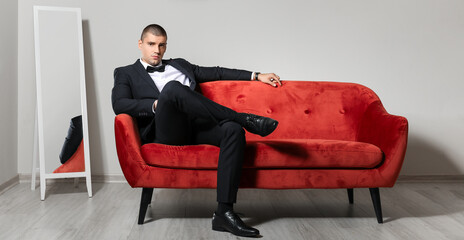 Handsome young man in elegant suit sitting on sofa indoors
