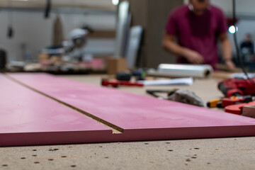 Furniture manufacture. Edge of pink furniture board close-up on workbench during production of cabinet furniture on blurred background of interior of furniture workshop