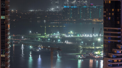 Aerial view to Dubai marina skyscrapers with construction site and Palm Jumeirah Island on background night timelapse.