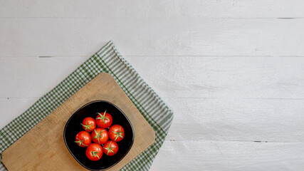 Top view of fresh ripe cherry tomatoes in small black bowl on a rustic white wooden table. Ingredients and food concept