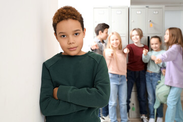 Bullied little African-American boy near wall at school