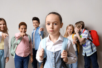 Bullied little girl and her classmates on light background - obrazy, fototapety, plakaty