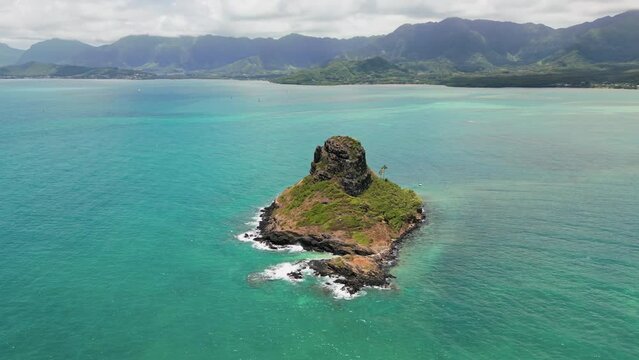 Aerial view of teal blue Pacific ocean with scenic high green mountains covered with rainforest and China Hat on Oahu Island, Honolulu, Hawaii. High quality 4k footage