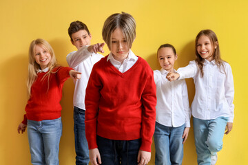 Bullied little boy and his classmates on yellow background
