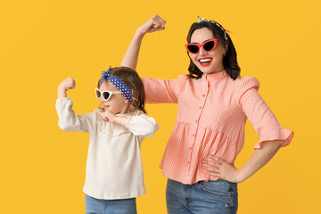 Beautiful pin-up woman and her daughter in sunglasses showing muscles on yellow background