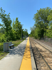 Bench in the park. Public bench in a railway station. Seatings near a litter garbage can. Train station. Furniture for resting while waiting for public transport.  Railroad tracks in the countryside.